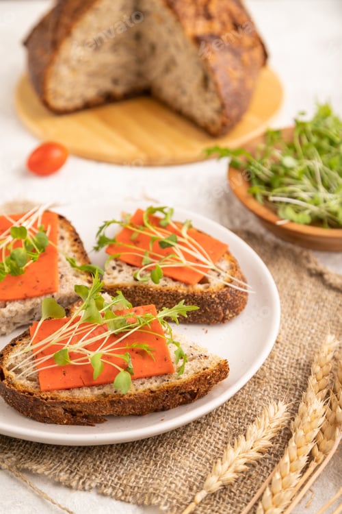 Preview: Grain bread sandwiches with red tomato cheese and microgreen on gray, side view, selective focus.