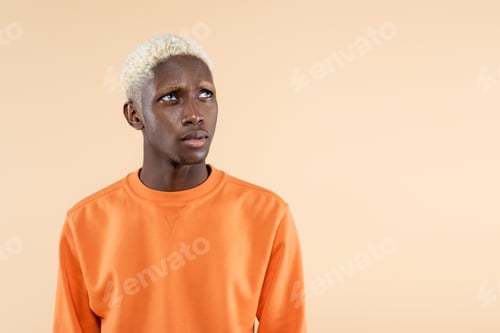 Preview: dreamy african american man in orange sweatshirt looking away isolated on beige
