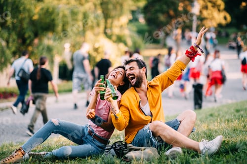 Preview: Young happy couple enjoying a park with beer in hand during the summer