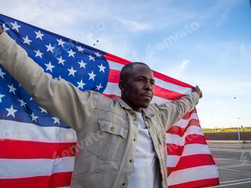 Preview: Handsome black Spanish male with hands up holds a flag of the USA behind him