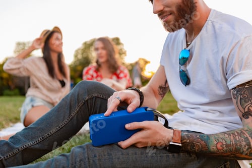 Preview: company of friends having fun together in park listening to music