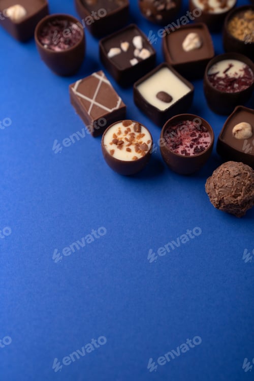 Preview: close up artisanal chocolate pralines truffles on vivid blue backdrop textures creamy fillings nuts