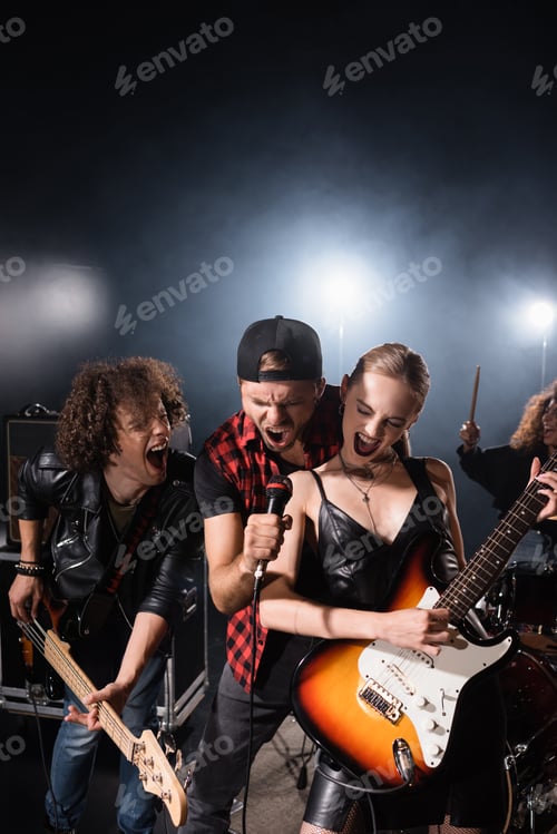 Preview: KYIV, UKRAINE - AUGUST 25, 2020: Vocalist shouting in microphone while standing near rock band