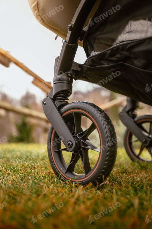 Preview: Detail on wheels of outdoor stroller on green mountain meadow in winter