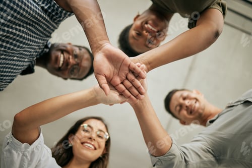 Preview: Cheerful group of colleagues putting hands together in the office. Below view of team stacking hand