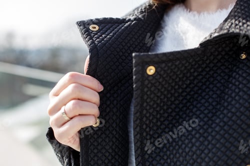 Preview: A woman with long hair holds the collar of a black coat, part of the coat with hands