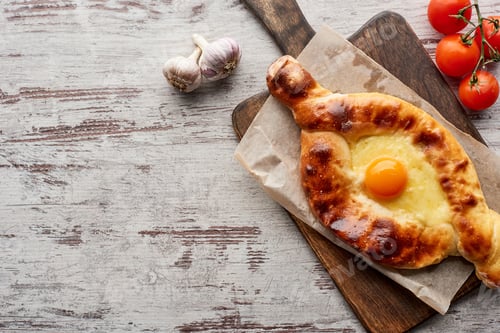 Preview: Top view of adjarian khachapuri with tomatoes and garlic on table