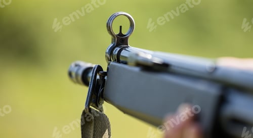 Preview: Shotgun in man' s hand. Front side of weapon with close up view on blurred nature background.