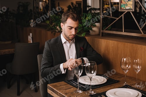 Preview: handsome man in suit waiting for girlfriend in restaurant and looking at watch