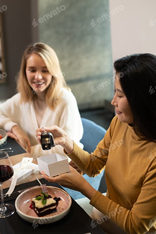 Preview: Young Asian female taking present out of small giftbox and showing it to friends