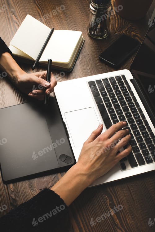 Preview: close-up partial view of person using laptop and graphics tablet at workplace