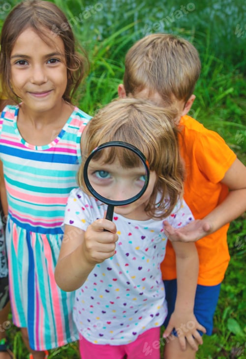 Preview: Children look at a magnifying glass on the nature. Selective focus.