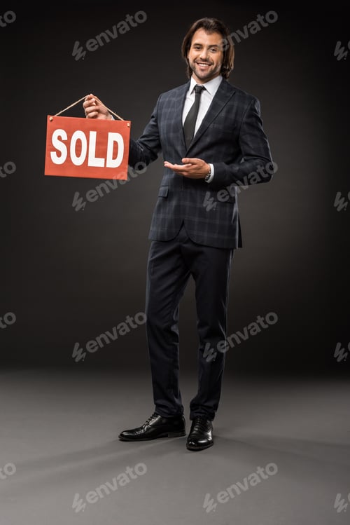 Preview: professional young businessman showing sold sign and smiling at camera on black