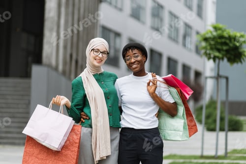 Preview: Two multiethnical girls, walking down the old city street after shopping, carrying colorful bags