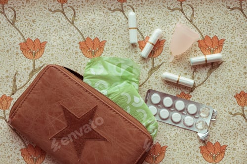 Preview: Female hygiene products lay out on a bed. Paracetamol, Sanitary pad, tampon, Chocolate,