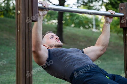 Preview: Athletic guy trains in the fresh air and performs lying down pull ups bar exercises
