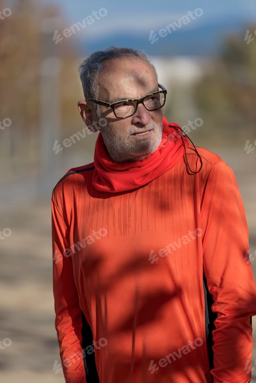 Preview: Active senior runner in orange sweatshirt in nature resting.