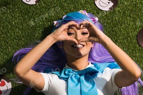 Preview: Smiling asian anime girl lying on grass and showing heart sign