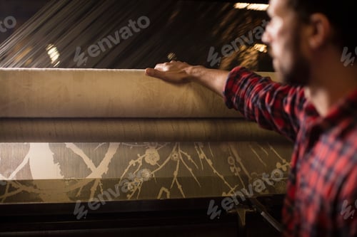 Preview: Young male weaver with lace roll on old weaving machine in textile mill