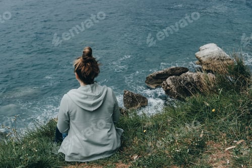Preview: Young woman in a green jacket looks at the sea from the mountain
