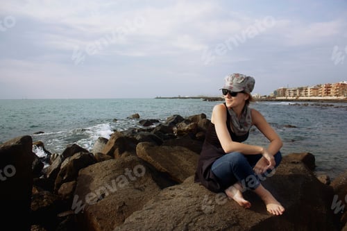 Preview: Young girl sitting on big rocks by the sea