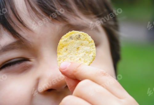 Preview: Cropped shot kid showing potato chips,happy boy looking at fired potato,Child eating potato crisp