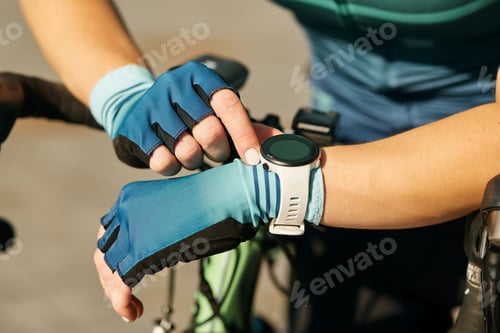 Preview: Close up shot of hands of professional female cyclist in cycling garment using smartwatch, checking