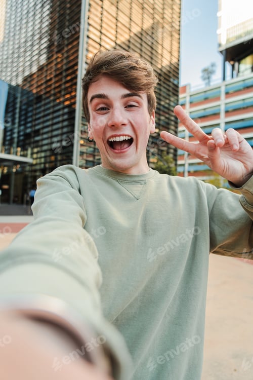 Preview: Vertical. One confident young male smiling taking a selfie portrait with a cell phone. Friendly