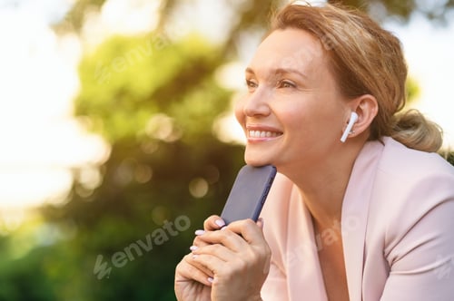 Preview: Close-up portrait of a smiling woman with smartphone on the street.