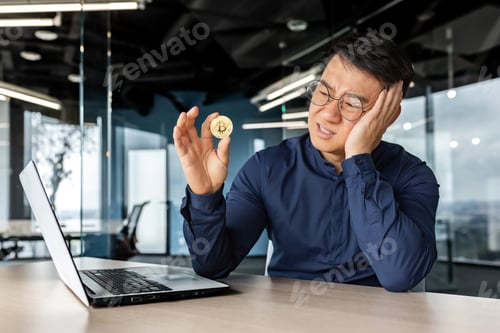Preview: Frustrated asian businessman investor holding crypto currency bitcoin in hands, man working inside