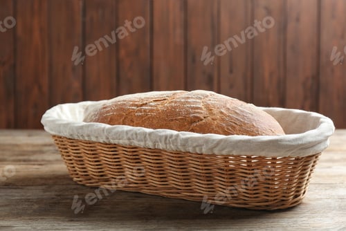 Preview: Loaf of tasty fresh bread in wicker basket on wooden table