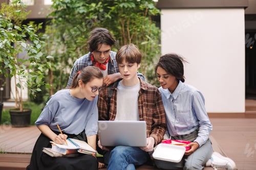Preview: Group of young students sitting on bench with books and laptop on knees and studying together