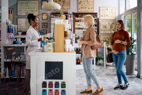 Preview: Happy black pharmacist serving her customers in a pharmacy.
