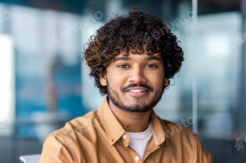 Preview: Close-up portrait of a young smiling Indian man sitting and working in the office, looking