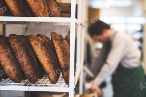 Preview: Artisan bakery making special sourdough bread, racks of bread and a baker in the background.