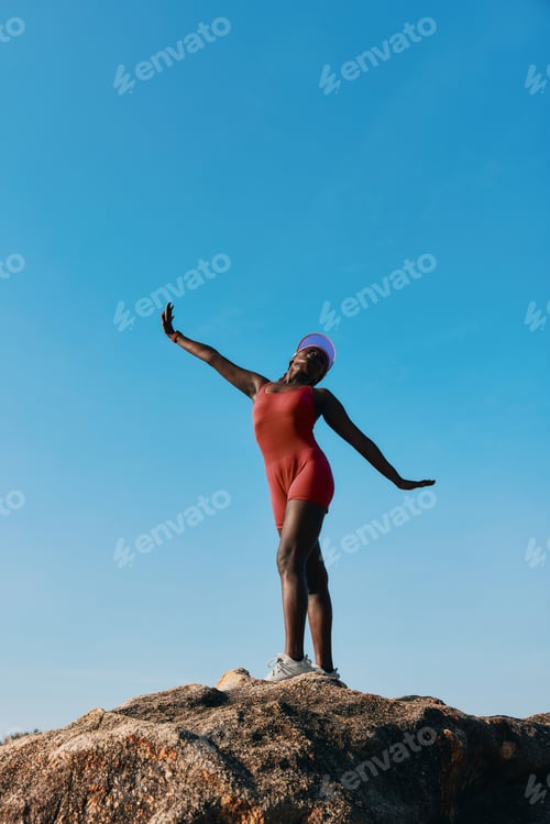 Preview: A confident person striking a pose on a rock against a clear blue sky, showcasing a joyful