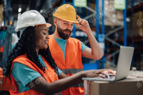 Preview: Multiracial man and woman collaborating on laptop for warehouse tasks