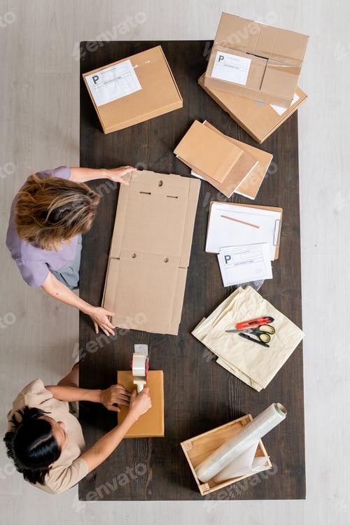 Preview: Top view of two managers of online shop packing orders of clients into boxes