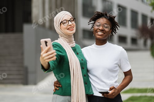 Preview: Charming women, one in hijab and other her african american friend taking selfie.