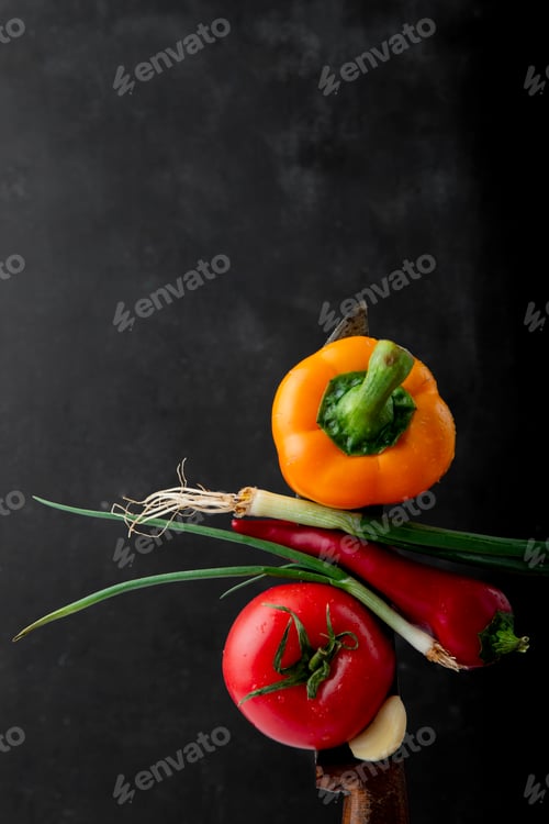 Preview: top view of vegetables as tomato, pepper, scallion and garlic on knife on black background with copy