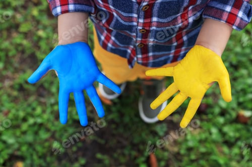 Preview: Little boy with hands painted in Ukrainian flag colors outdoors, top view. Love Ukraine concept