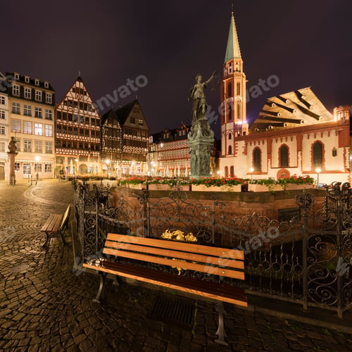 Preview: Historic European square illuminated at night with a statue and bench in the foreground