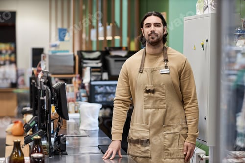 Preview: Man working in supermarket and looking at camera standing by cashiers desk
