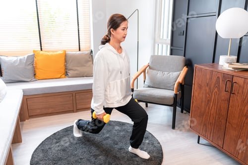 Preview: Asian woman is doing yoga exercise with dumbbell on side body during workout in living room at home