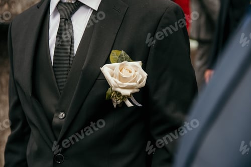 Preview: Selective focus photo of white rose on groom's suit on wedding day.