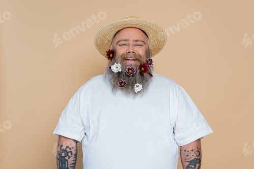 Preview: overweight man with decorated beard and straw hat smiling at camera isolated on beige