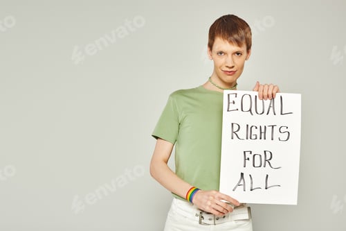 Preview: portrait of young queer activist wearing lgbt flag bracelet and holding placard with equal rights