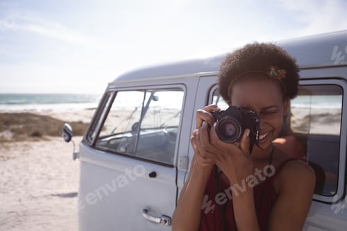 Preview: Woman using digital camera at beach against a camper van in background as well as ocean