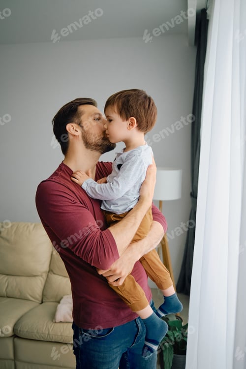 Preview: Caring father kissing his small son while holding him at home.