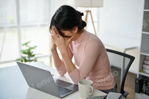 Preview: Stressed and frustrated Asian businesswoman covering her face and crying at her desk